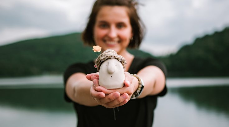 kobieta trzyma figurkę ceramiczną, która jest na pierwszym planie fotografii